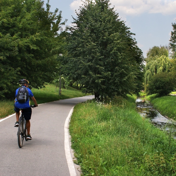 Photographie d'un individu roulant à vélo sur une piste cyclable au bord d'un cours d'eau
