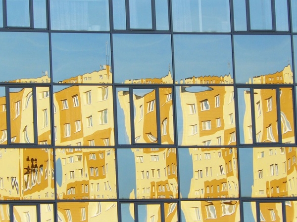 Photographie d'une paroi vitrée réfléchissant une immeuble jaune