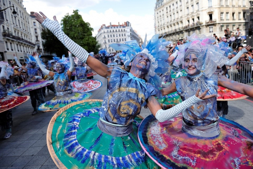 Photo de deux personnes en costumes et aux visages colorés dansant ensemble et souriant sur la rue de la République
