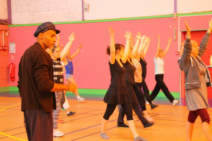 Fred Bendongué animant une répétition de danse pour le Défilé de la Biennale, en arrière plan, des personnes marchant ensemble dans des lignes avec les bras tendus haut dans l'air