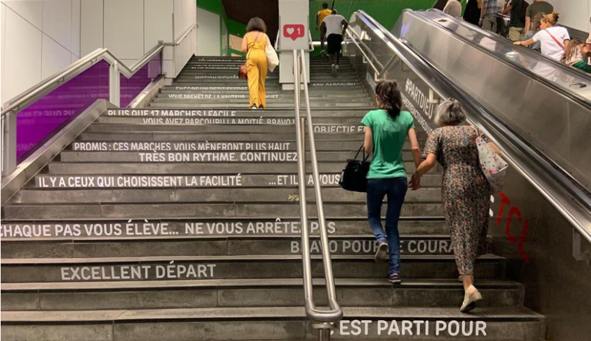 Photographie de marches d'escalier où des stickers indiquent "Vous avez parcouru la moitié bravo !" ; "Promis : ces marches vous mèneront plus haut" ; "très bon rythme. Continuez" ; "Il y a ceux qui choisissent la facilité ...Et il y a vous" ; Chaque pas vous élève... Ne vous arrêtez pas" ; "Excellent départ"
